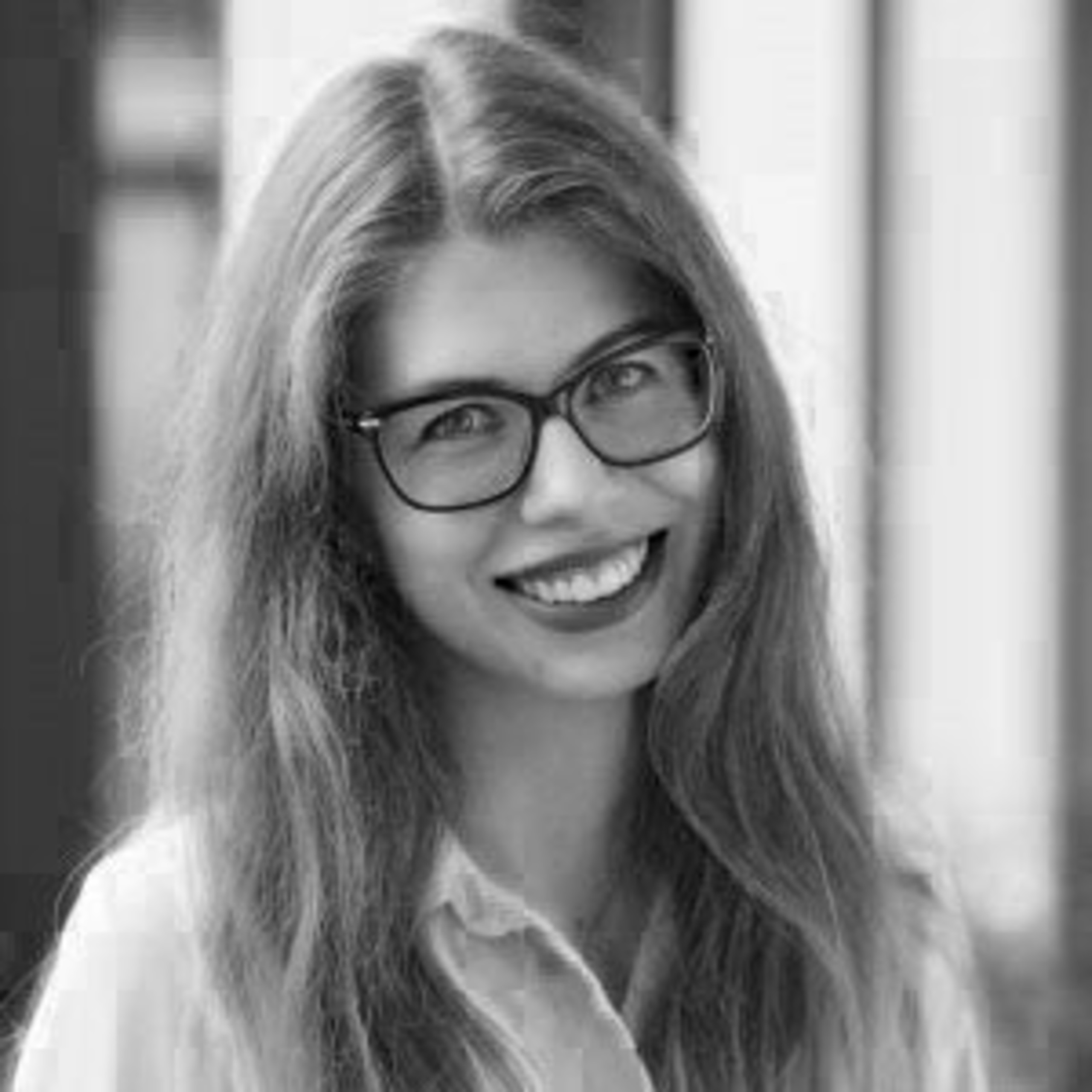 Juodai baltas jaunos moters portretas: ji šypsosi, vilki šviesius drabužius ir dėvi akinius, o ilgi plaukai laisvai krinta ant pečių.