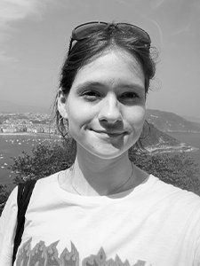 Mergina su baltais mar&scaron;kinėliais ir akiniais ant galvos daro asmenukę nuo auk&scaron;tos apžvalgos aik&scaron;telės, fone matyti pajūrio miestas su įlanka, laivais ir kalvomis tolumoje.